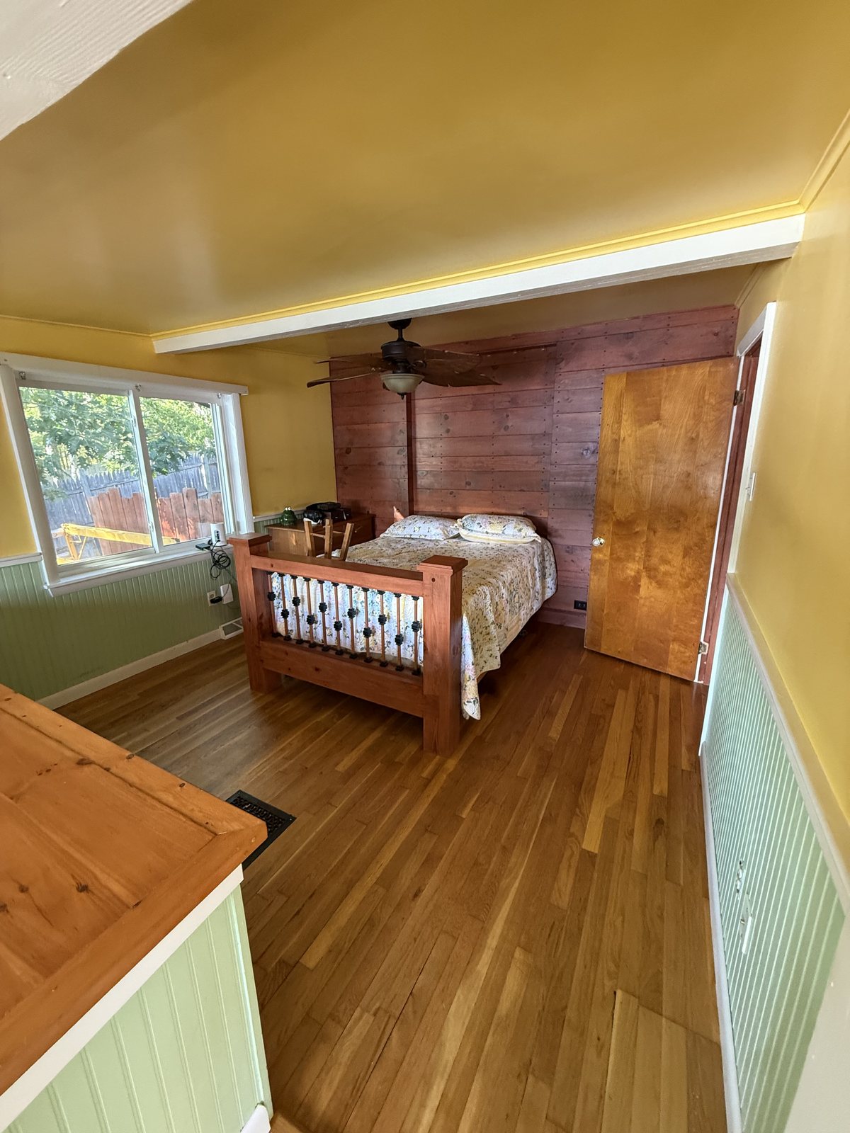 Bedroom with a cedar plank accent wall, a made wooden bed and oak floors after a house cleaning visit