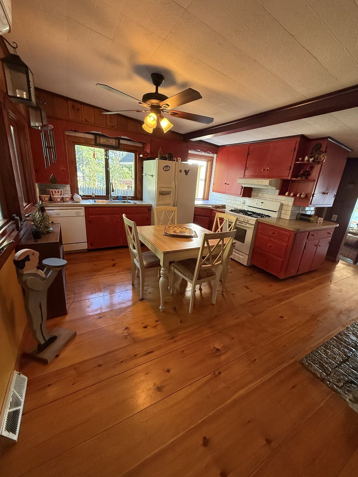 Farmhouse kitchen with red painted cabinets, wide pine floorboards and a gas range, wiped down and floors cleaned after a house cleaning visit