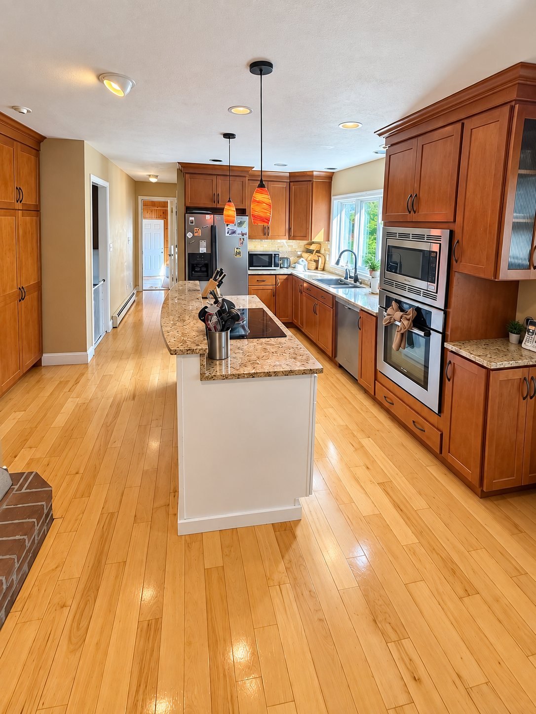 Open kitchen with cherry cabinets, a granite island and light maple floors, counters cleared and floors cleaned after a house cleaning visit