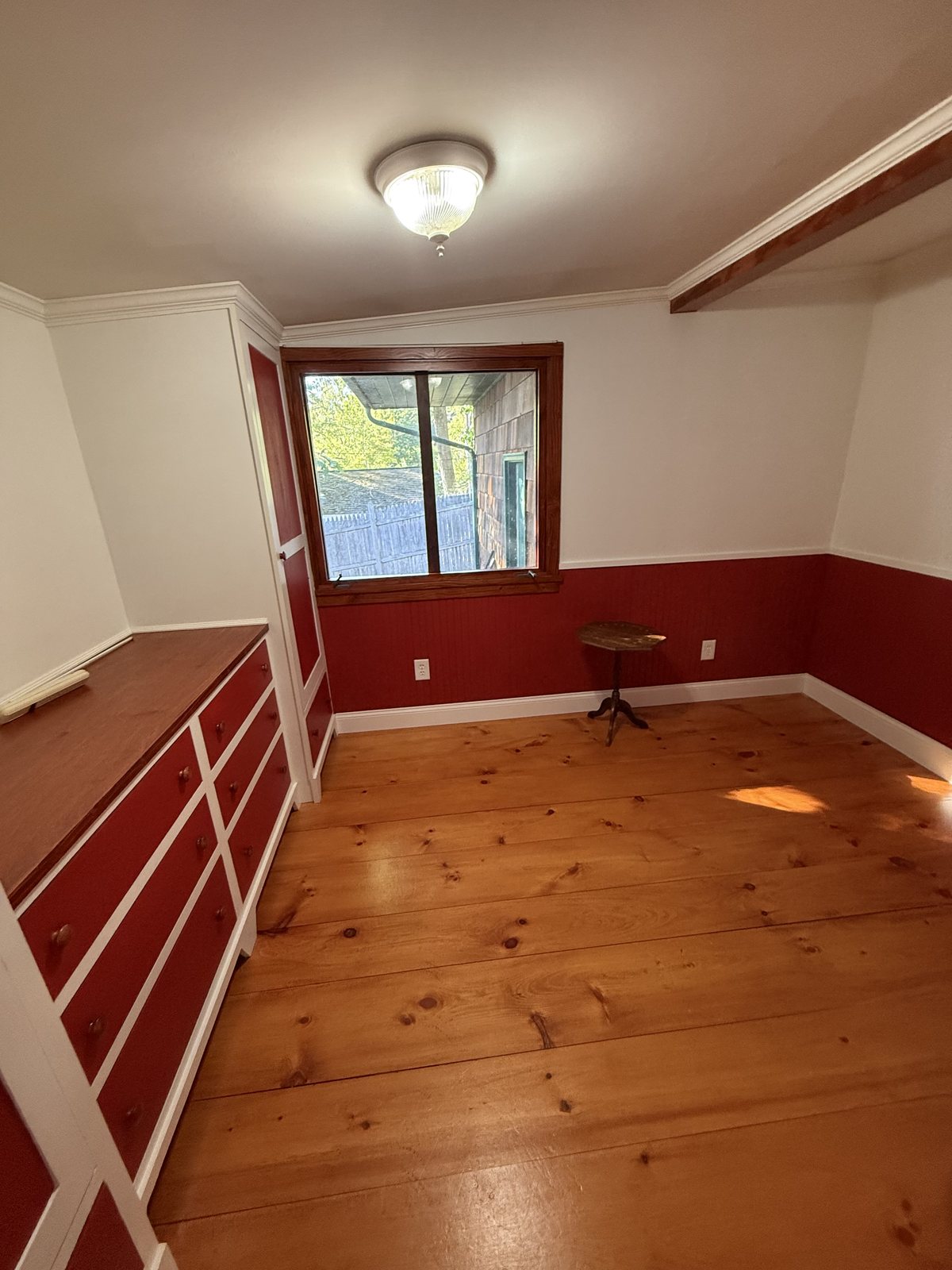 Empty bedroom with red beadboard wainscoting, a built-in dresser and wide pine floors, cleaned and ready for the next occupants